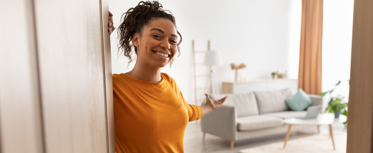 Young female homeowner opening her doors to welcome guests